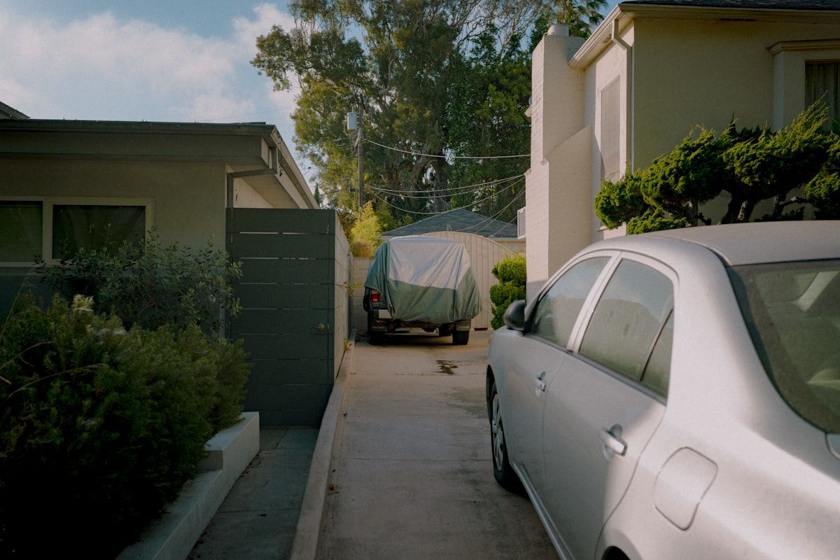 A roll-off dumpster sitting in a residential driveway beside a house, with one side close to the curb and another version placed at the edge of a quiet street, showing the contrast between private property placement and public right-of-way placement