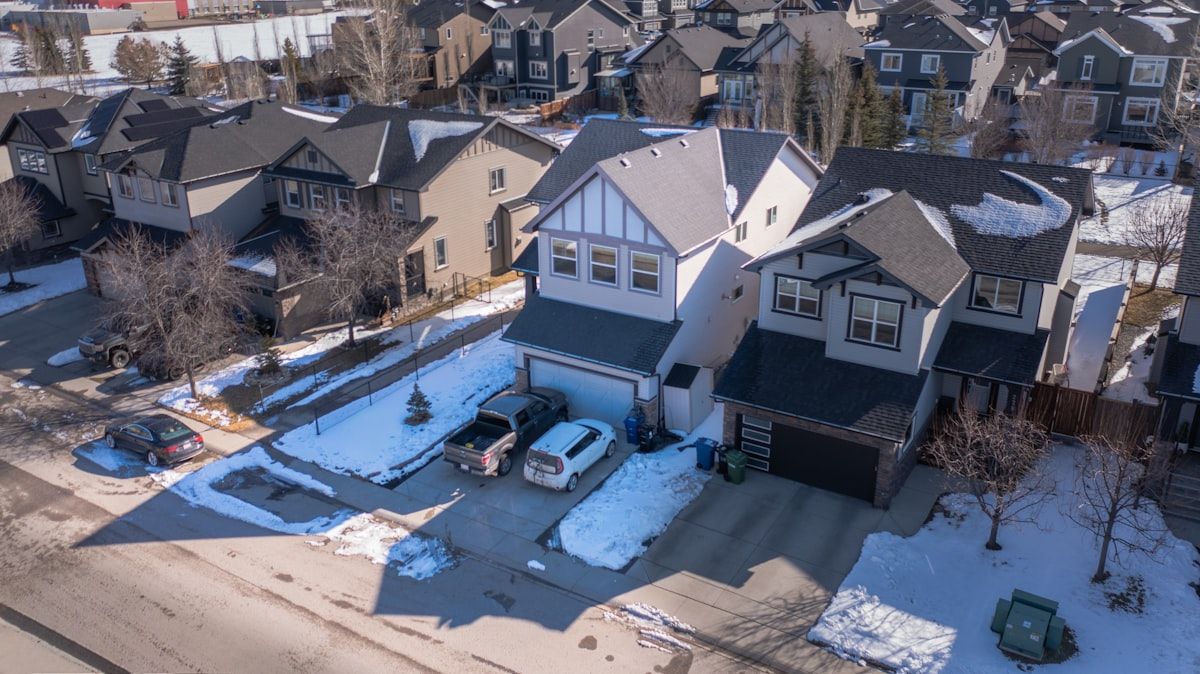 A suburban home with a dumpster sitting neatly on a driveway protected by wooden planks, alongside a street view with a curb and municipal permit paperwork clipped to a folder, showing the difference between private-property placement and public-street placement.