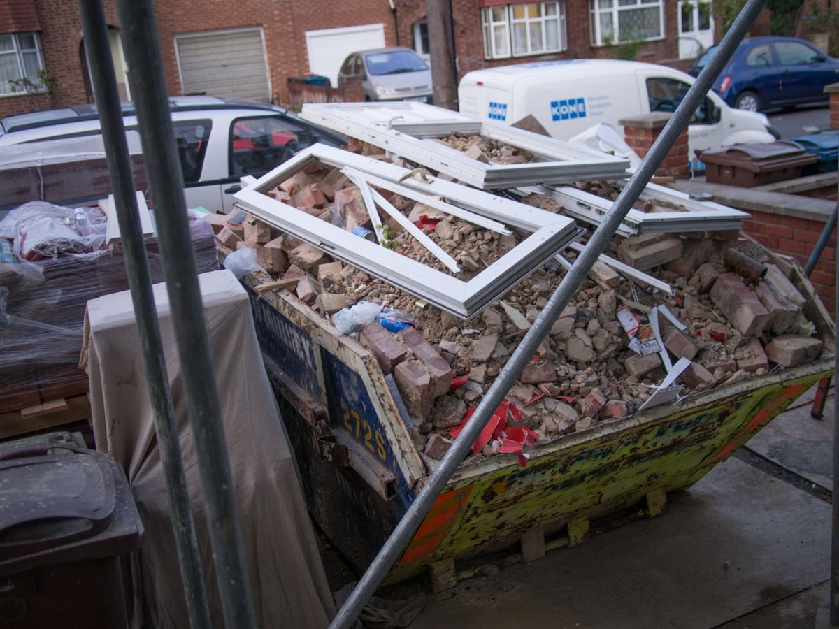 A dumpster filled with dense construction debris such as cracked concrete slabs, broken bricks, roofing shingles, and a small pile of dirt, with a few lighter items like cardboard and wood trim on top to show how heavy materials can quickly dominate the load.