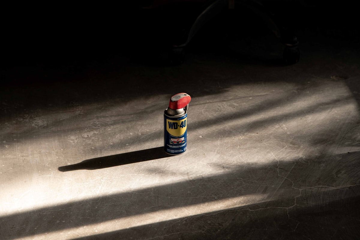A collection of restricted items arranged on a garage floor: a gasoline can, a propane tank, a half-full paint can, loose batteries, an old television, a microwave, and a refrigerator with the door open, all separated from a large construction debris pile